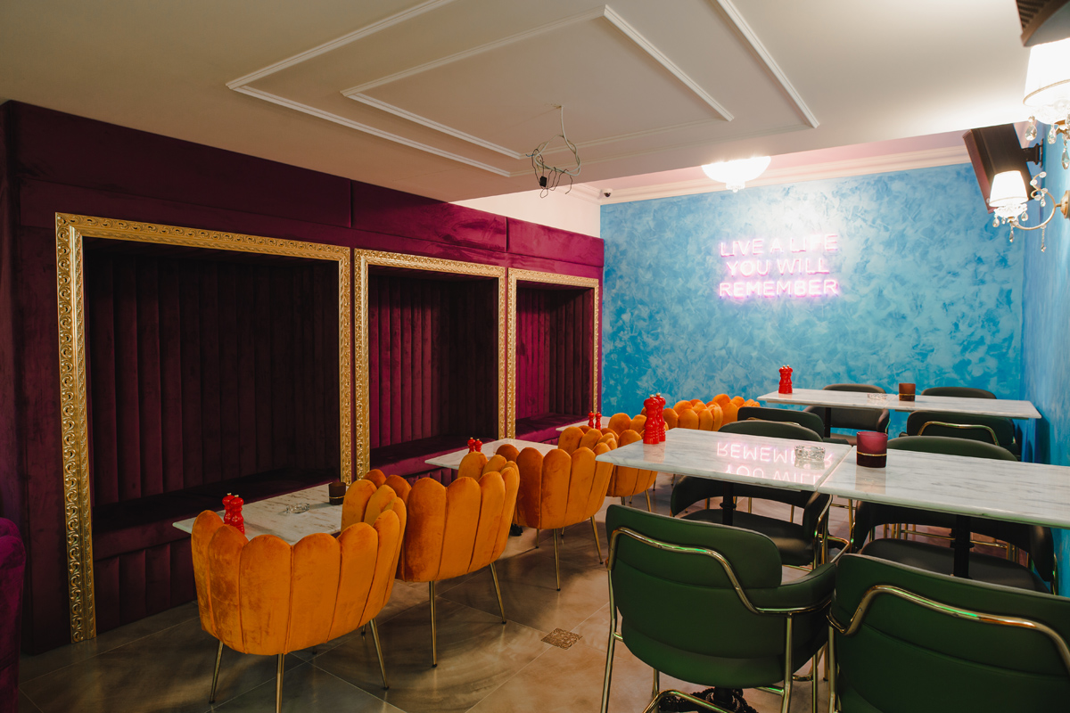 Enterijer restoranskog bara ,narandžaste i viseće zelene stolice pored plavog zida i elegantnog prostora gdje se može sjeti u zidu u bordo boji