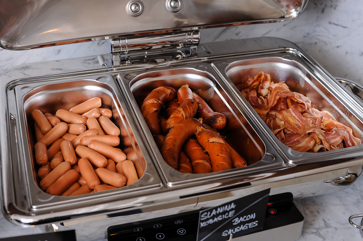 Viršle, kobasice i slanina u ponudi za doručak koji se nalazi u metalnim posudama u banquet restoranu hotelu Integra